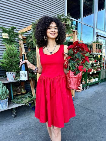 Woman in a sleeveless red dress holding a poinsettia plant at a plant shop