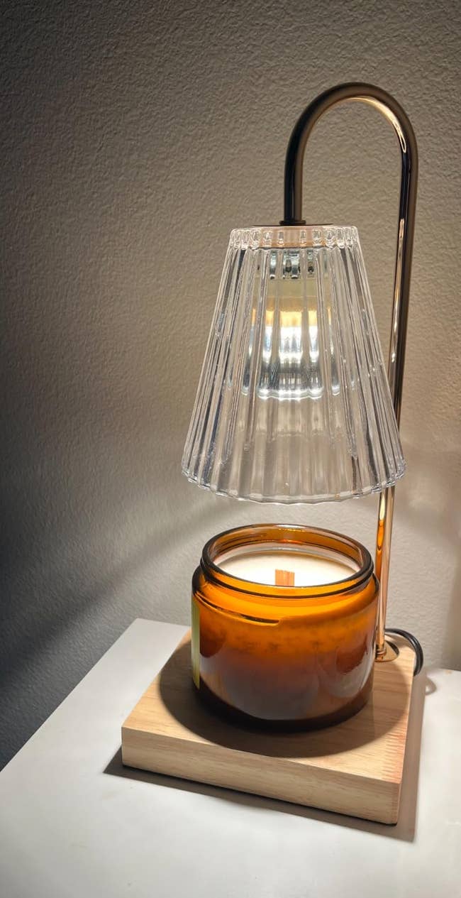 Glass candle warmer lamp connected a table, featuring a sleek arching plan with a ribbed shade, adjacent to a tiny instrumentality with 2 lipstick tubes