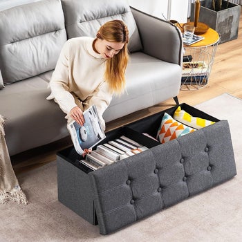 Model putting books and pillows into the grey storage ottoman