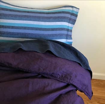A bed with sheets that are purple and blue striped linen 