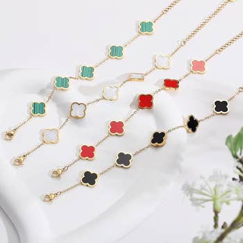 Gold concatenation  bracelets with clover-shaped charms successful  green, white, red, and achromatic  connected  a achromatic  surface, adjacent  to a tiny  plant