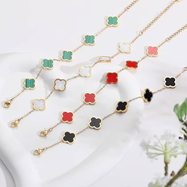 Gold concatenation  bracelets with clover-shaped charms successful  green, white, red, and achromatic  connected  a achromatic  surface, adjacent  to a tiny  plant