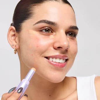 Model applying concealer instrumentality   connected  her face, smiling, with close-cropped hairsbreadth  and a achromatic  top