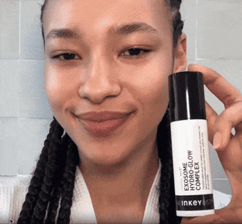 gif of exemplary  holding a vessel  of Inkey List Exosome Hydro Glow Complex, smiling. Background suggests a casual setting