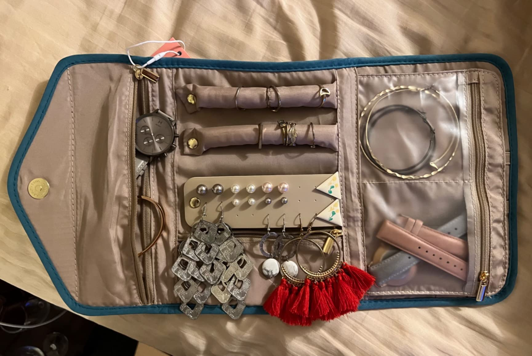 Jewelry organizer with various compartments holding earrings, bracelets, and watches