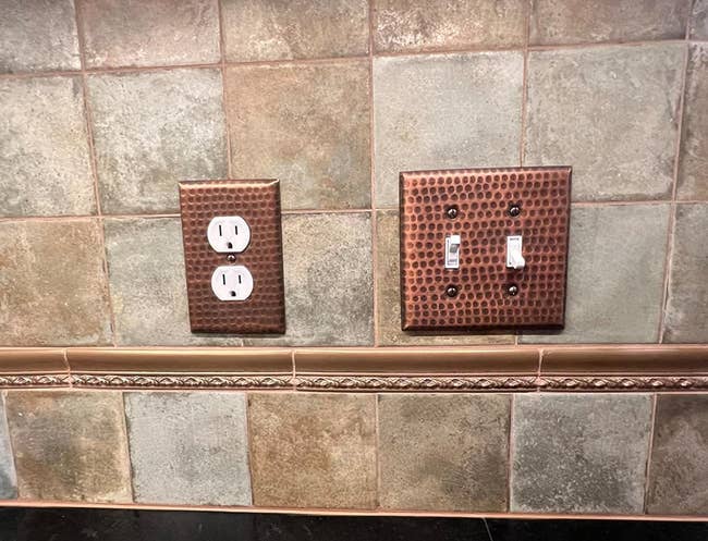 two copper hand hammered switch plates on a wall