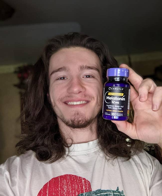 A reviewer smiling while holding up the bottle of melatonin tablets
