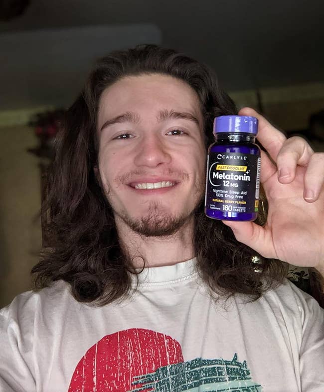 A reviewer smiling while holding up the bottle of melatonin tablets
