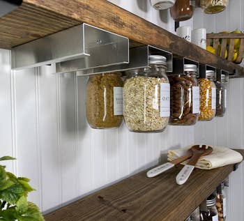 photo of jar holders installed under floating shelves and holding various filled mason jars