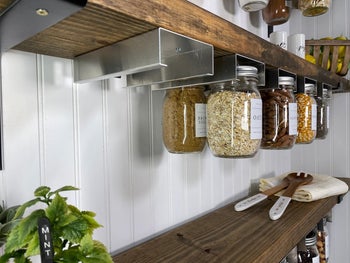 photo of jar holders installed under floating shelves and holding various filled mason jars