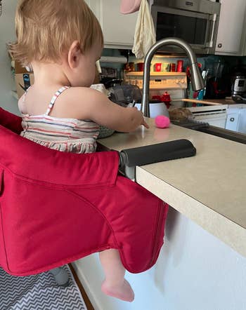 side view of reviewer's child in a red high chair at a kitchen bar