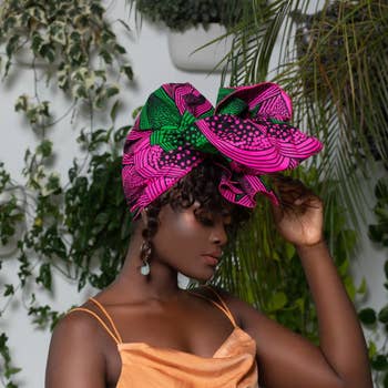 model in vibrant headwrap and orange dress posing with plants in background