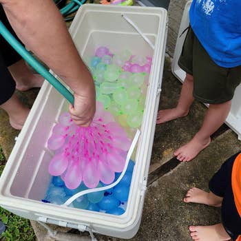 Person filling colorful h2o  balloons successful  a cooler portion    children watch; outdoor amusive  enactment   setup