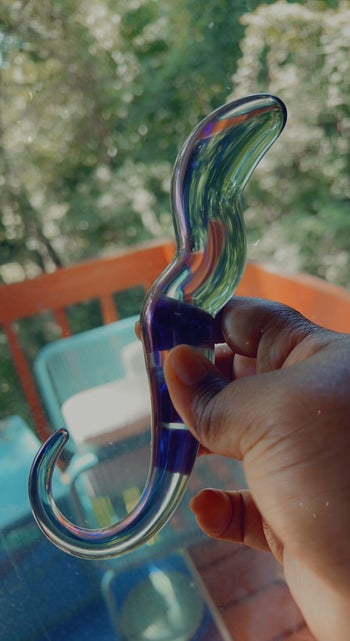 Hand holding iridescent dildo with curved handle