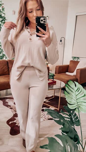 Person in a casual beige button-up shirt and matching pants taking a mirror selfie
