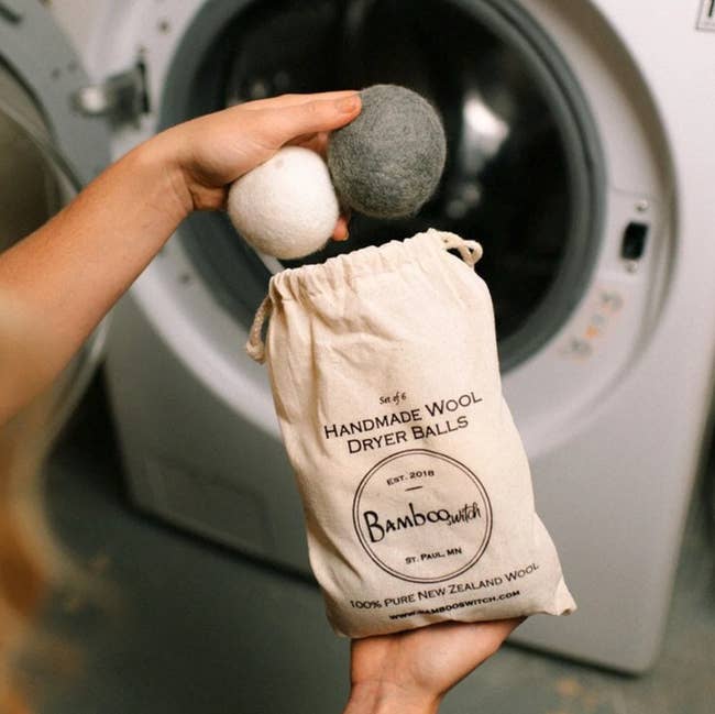 a model holding two dryer balls and the storage bag in front of a dryer