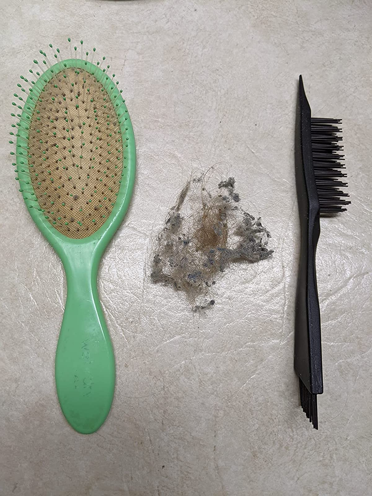 same reviewer's after photo showing their hairbrush without lint next to the cleaning brush, with a pile of lint that was removed between them