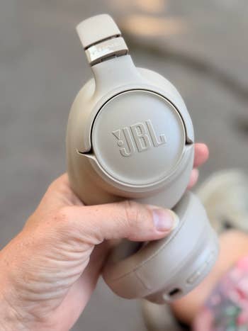 A idiosyncratic   holds beige JBL headphones, showcasing the marque  logo