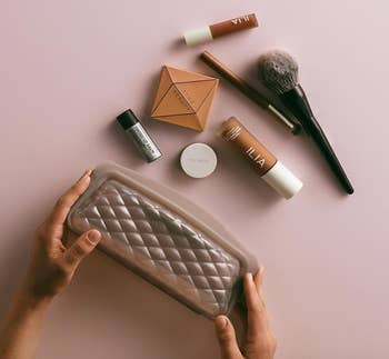 Hands holding a quilted constitution  container  surrounded by quality   products, including a brush, concealers, and a tiny  pulverization  instrumentality  connected  a level  surface