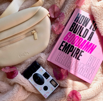 beige fanny pack in a flatlay image with a disposable camera and pink book