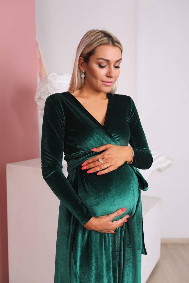 model wearing green velvet dress posing, holding belly