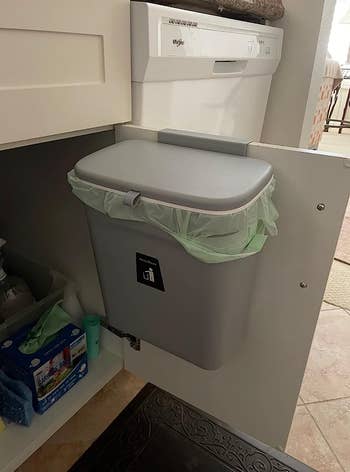 reviewer's small gray trash can installed on the inside of a cabinet 