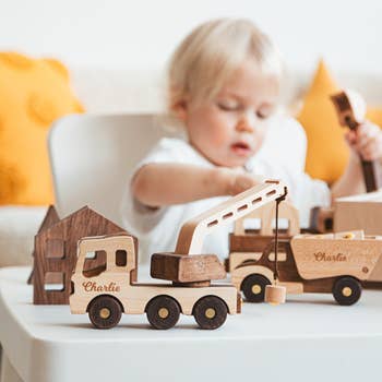 A child plays with wooden toy trucks featuring the name 