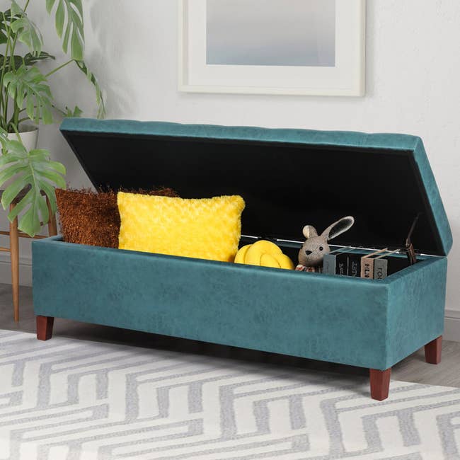 the vegan leather ottoman in a teal blue opened to show books pillows and toys inside