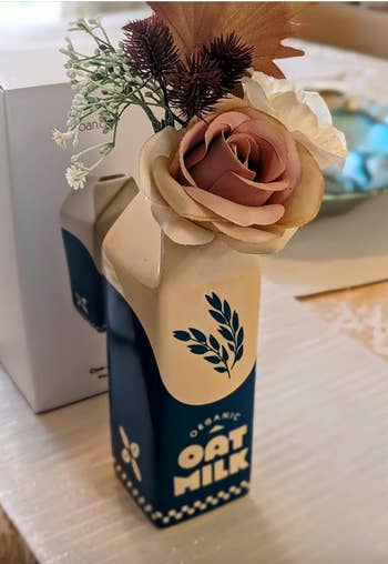 Decorative organic oat milk carton used as a vase with artificial flowers on a table