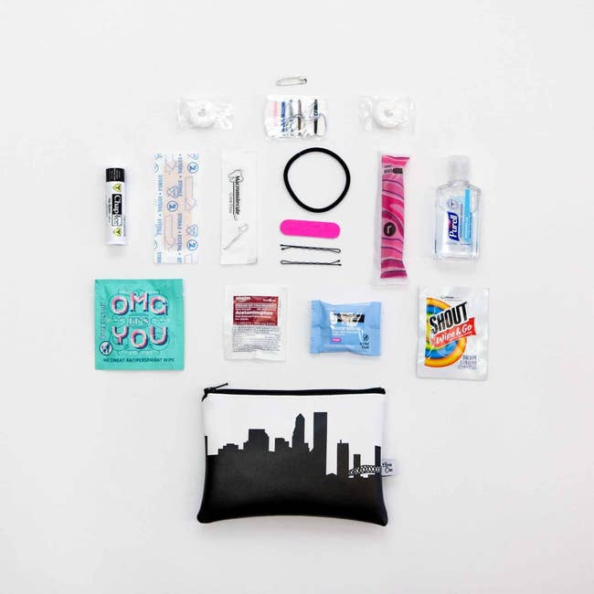 A small white faux leather pouch with a black skyline print surrounded by a mix of travel-sized toiletries and on-the-go essentials 