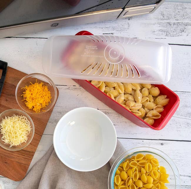 Kitchen counter with grated cheese, pasta, milk, and a microwave cooking container