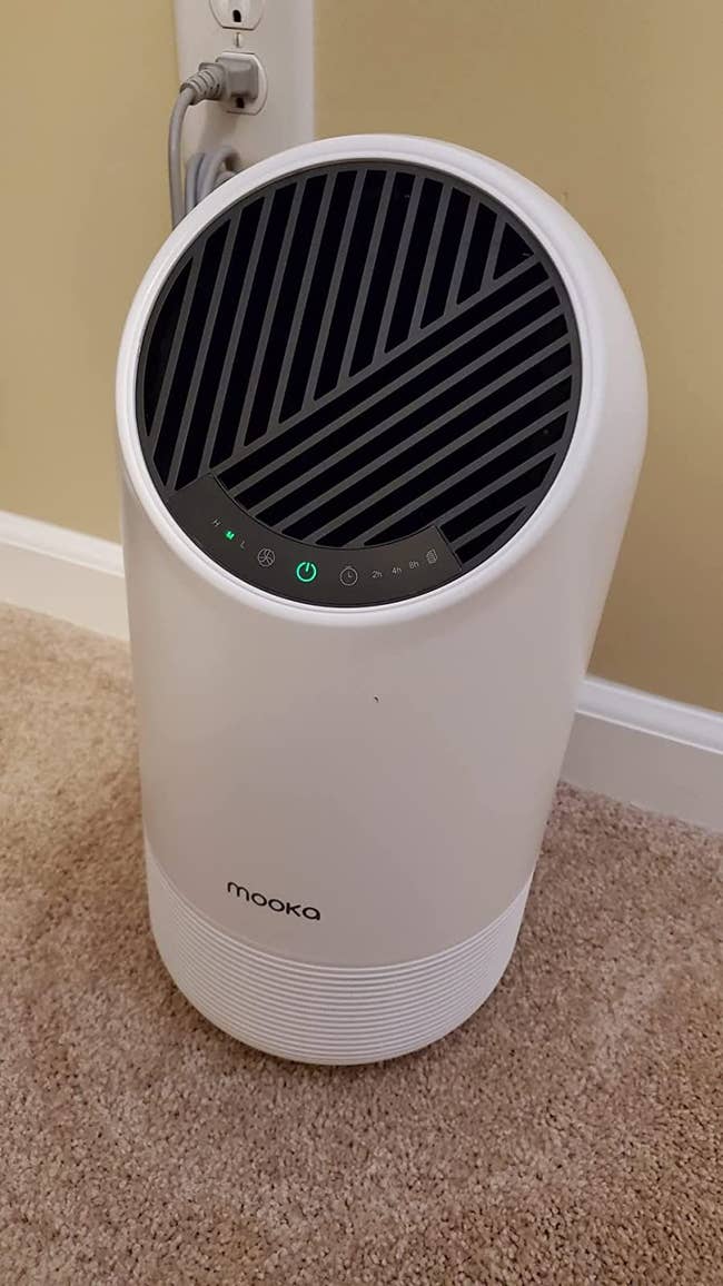 Reviewer image of small white and black air purifier with small lit up digital display screen on top of carpet