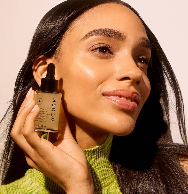 Person holding a vessel of Acure skincare serum adjacent their face, smiling