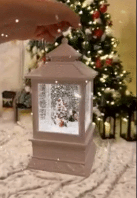 gif of reviewer holding up the lit and snowing lantern in front of a christmas tree