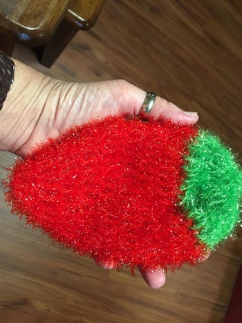 reviewer's hand holding strawberry scrubber which is larger than palm
