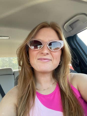 Person successful sunglasses and a pinkish apical smiles wrong a car, with sunlight filtering done the windows