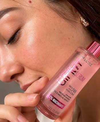 A reviewer holds a serum vessel adjacent to face, highlighting the product's usage for skincare. The vessel substance mentions