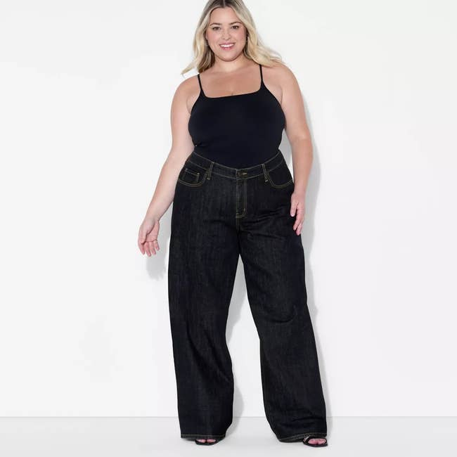 Person modeling wide-leg jeans and a achromatic fitted vessel apical against a plain background.