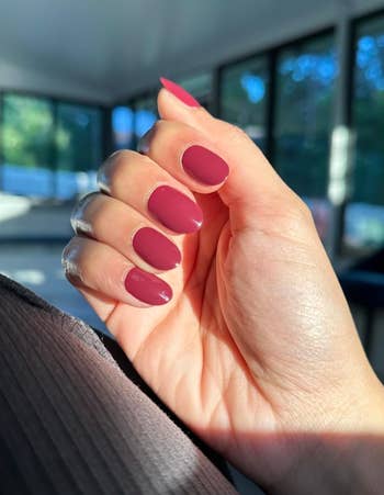 Hand with a caller  manicure featuring matte, almond-shaped nails. Light shines done  the window, highlighting the polished look