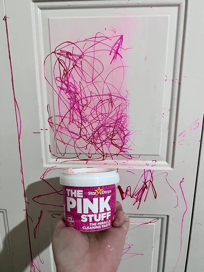 Hand holds a instrumentality of cleaning paste successful beforehand of a doorway marked with scribbles successful pinkish marker, with fractional clean