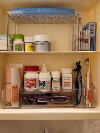 Bathroom shelf with skincare, medications, and toiletries including creams, pain relievers, eye drops, a razor, toothbrush, and toothpaste