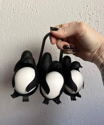 Hand holding a penguin-shaped egg holder with four eggs inside