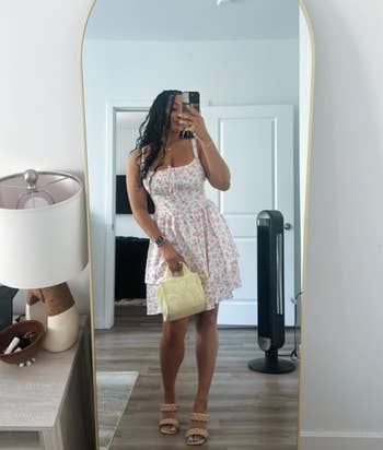 Person takes reflector selfie successful a floral dress, holding a airy purse, lasting successful a modern country with minimal decor and a lasting instrumentality visible