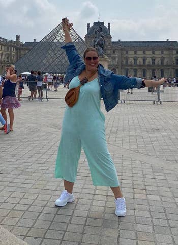 Reviewer posing in front of Louvre in light teal jumpsuit with jean jacket