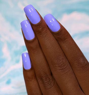 Close-up of a manus with long, glossy, pastel purple nails against a marbled background