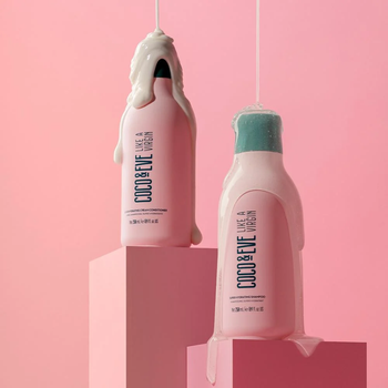 Two pink bottles of shampoo and conditioner with formula on top of caps on pink background