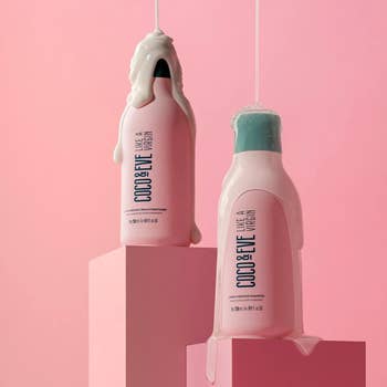 Two pink bottles of shampoo and conditioner with formula on top of caps on pink background