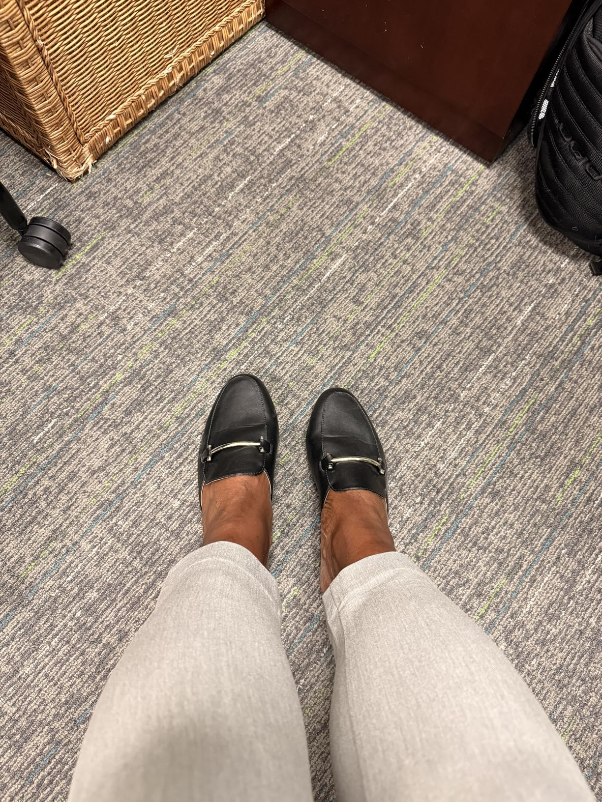 Black loafers with golden  buckles worn implicit    light-colored pants connected  a textured carpet floor
