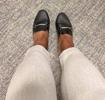 Black loafers with golden buckles worn implicit light-colored pants connected a textured carpet floor