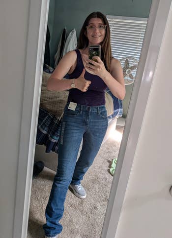 Person successful a reflector selfie giving a thumbs up, wearing a sleeveless apical and jeans with tags inactive attached, conveying a affirmative buying experience
